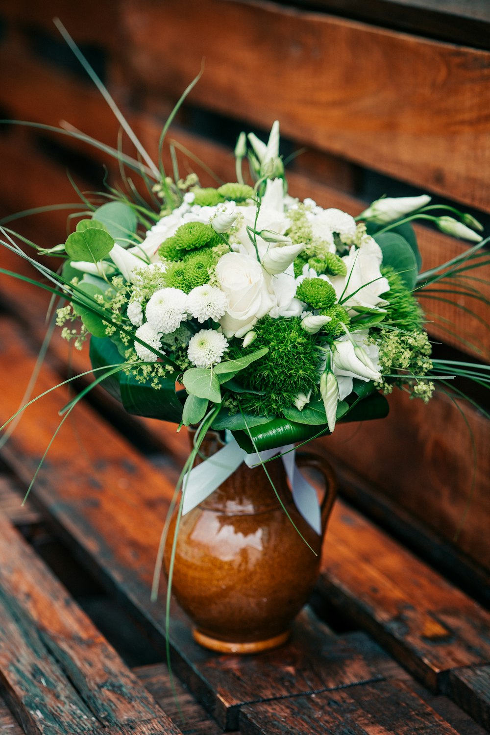 a vase filled with white flowers sitting on top of a wooden bench
