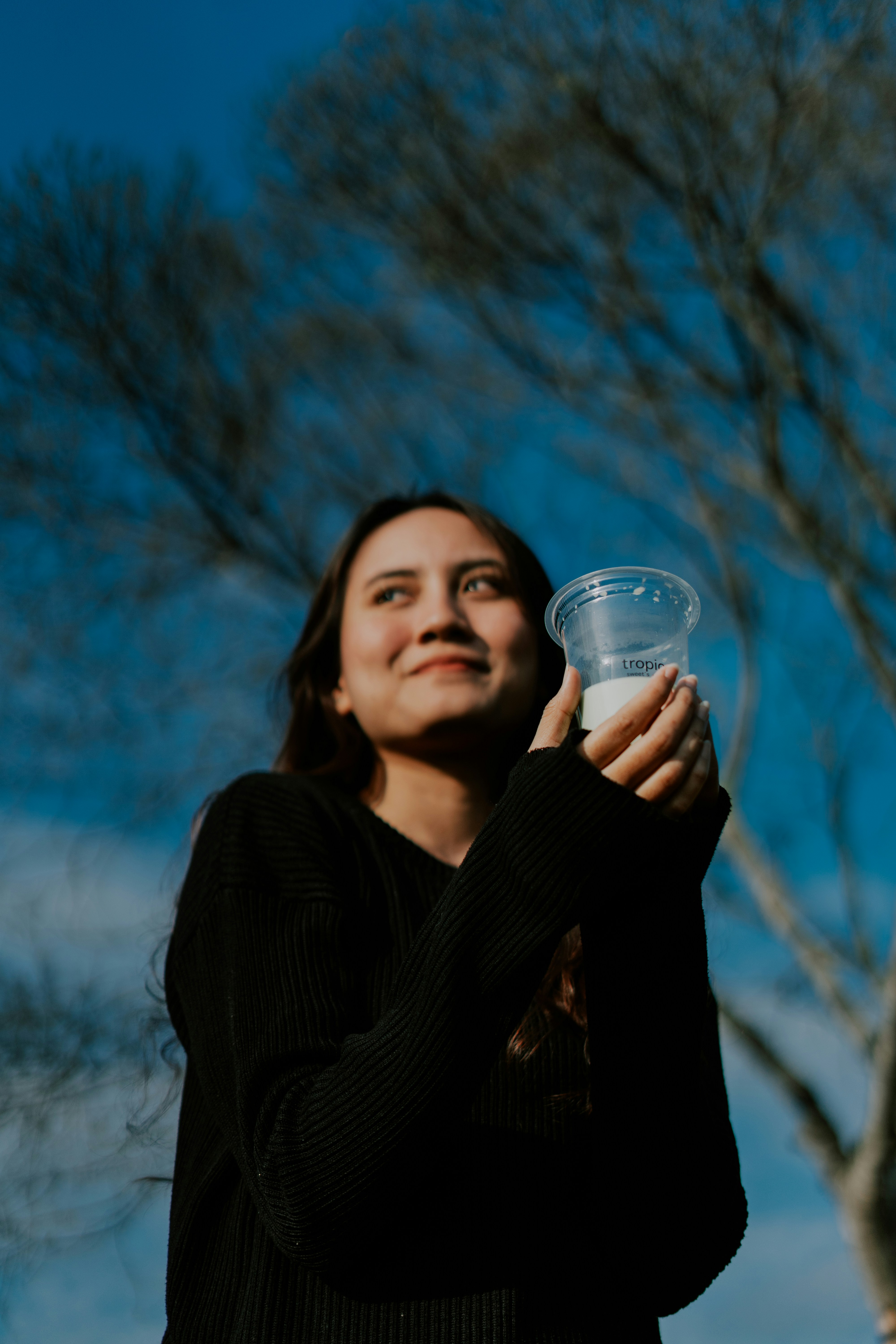 a woman holding a cup of water in front of a tree