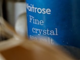 Close-up of a blue container labeled 'Waitrose Fine crystal sea salt,' with slightly blurred elements in the foreground creating a sense of depth.