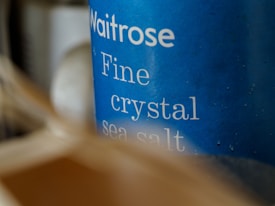Close-up of a blue container labeled 'Waitrose Fine crystal sea salt,' with slightly blurred elements in the foreground creating a sense of depth.