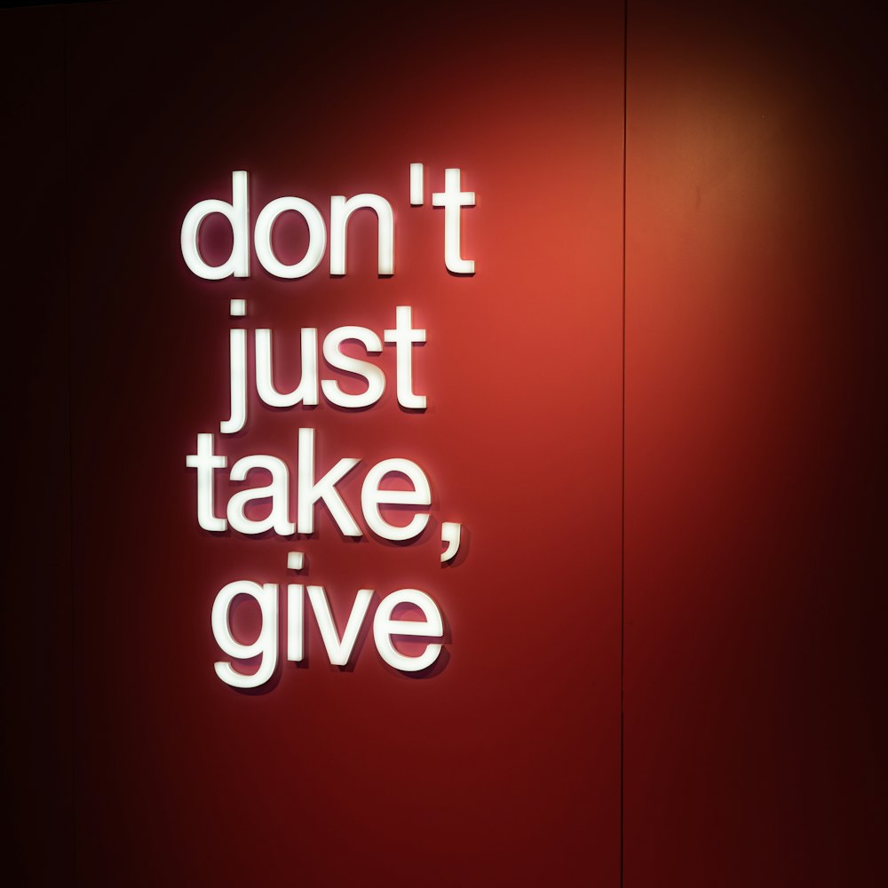 Eine rote Wand mit einer Leuchtreklame, auf der steht: Nicht nur nehmen, sondern geben