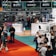 A busy exhibition booth featuring brands like Sony, Tamron, and DJI, where several people are interacting with product displays and browsing. The booth is well-lit with overhead lighting, and signs promote camera equipment and technology.