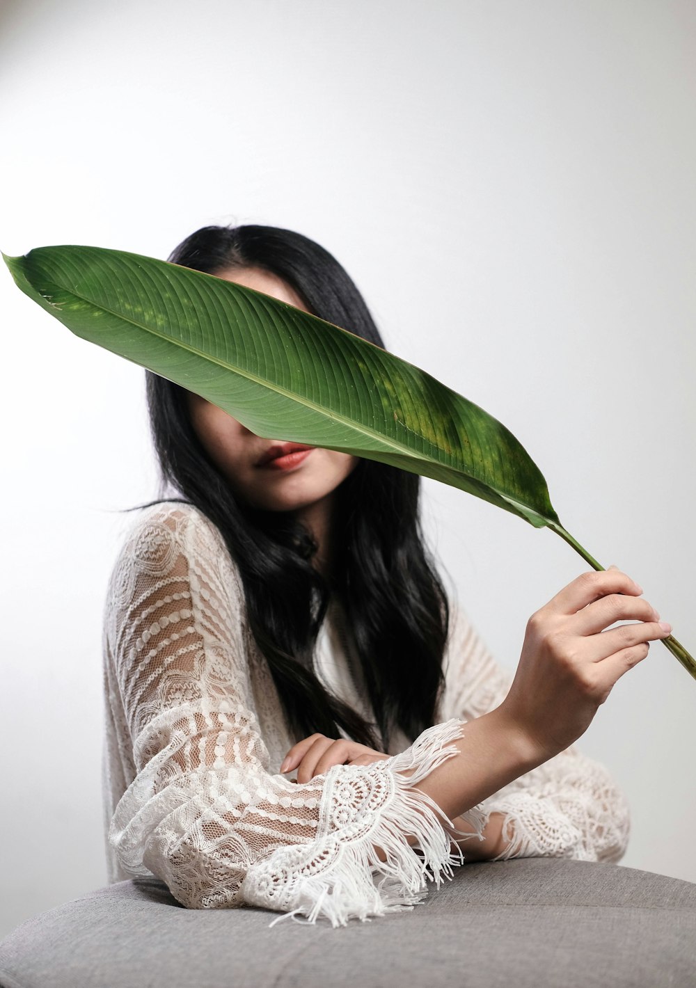 a woman holding a large green leaf over her face