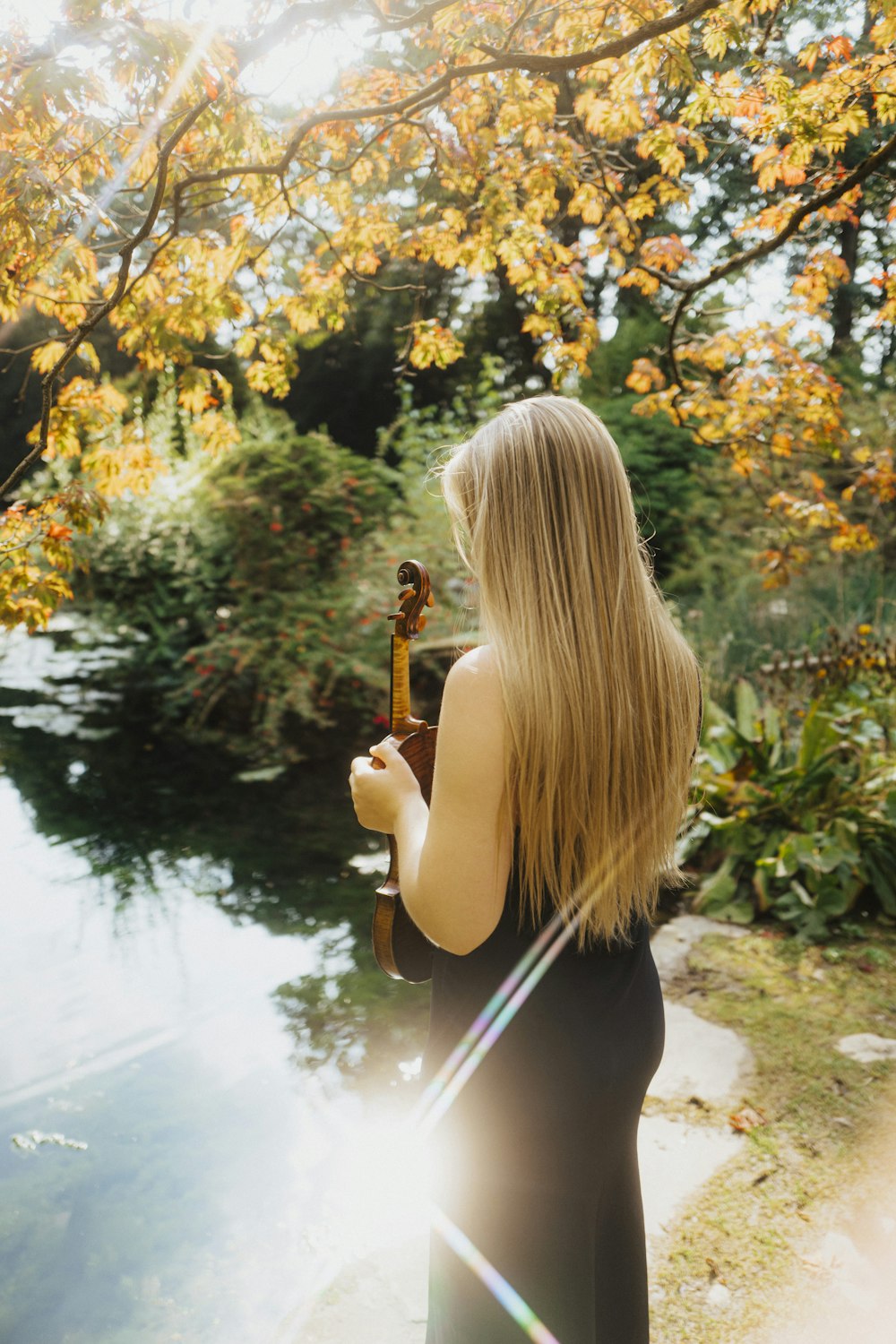 a woman standing next to a river holding a violin