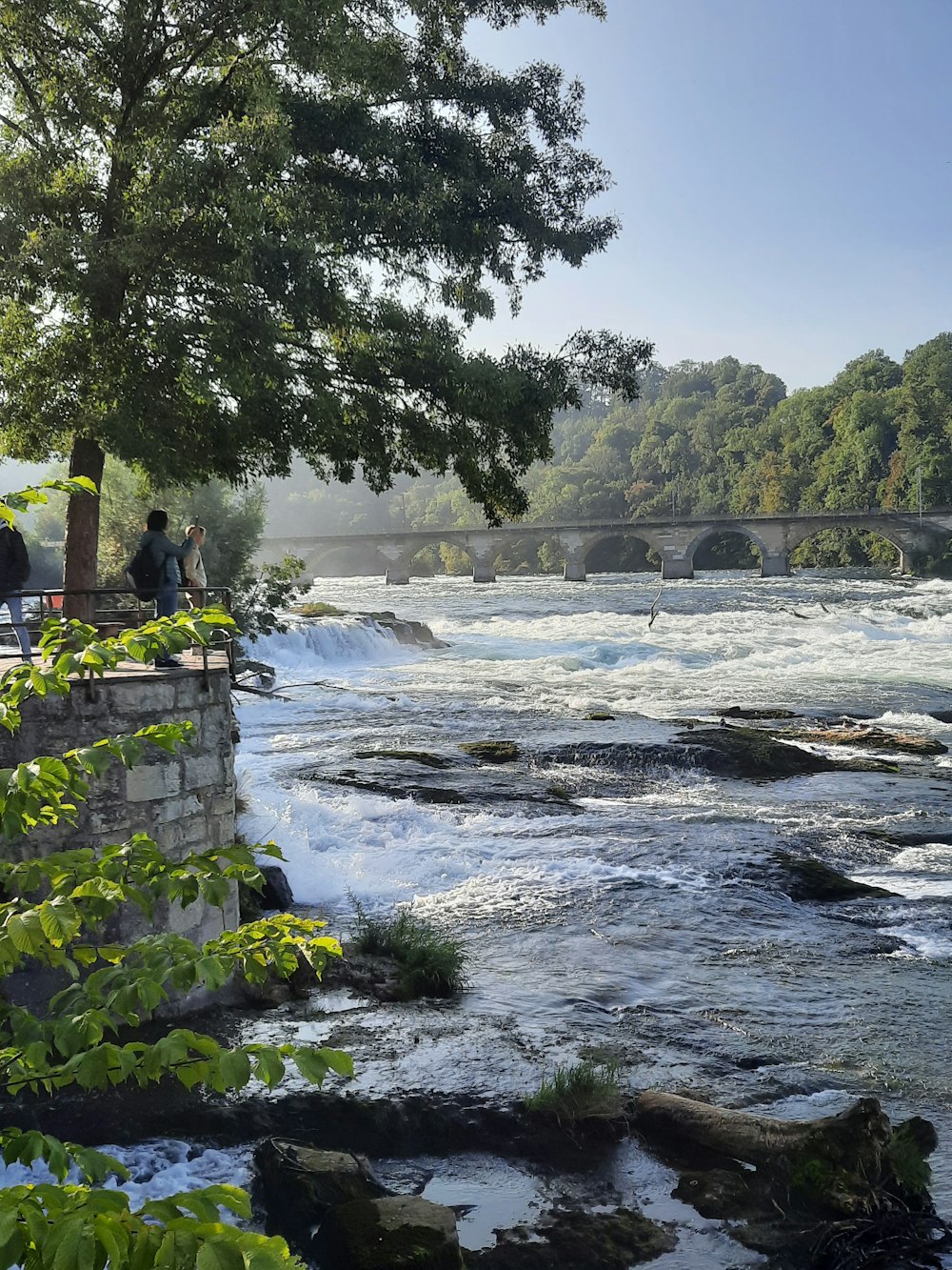 people sitting on a stone wall overlooking a river