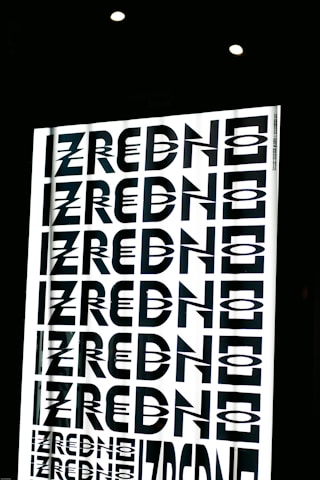 A graphic design featuring the repeated word 'ZREDNO' in bold, stylized black letters. The text appears in a mirrored pattern on a bright white background, creating an optical illusion effect. The image is framed by a dark border with circular lights at the top.