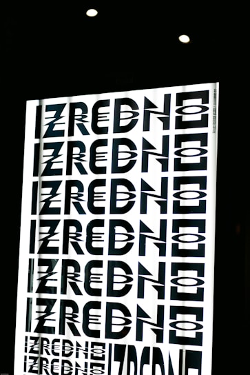 A graphic design featuring the repeated word 'ZREDNO' in bold, stylized black letters. The text appears in a mirrored pattern on a bright white background, creating an optical illusion effect. The image is framed by a dark border with circular lights at the top.