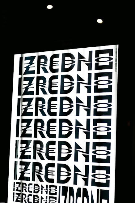 A graphic design featuring the repeated word 'ZREDNO' in bold, stylized black letters. The text appears in a mirrored pattern on a bright white background, creating an optical illusion effect. The image is framed by a dark border with circular lights at the top.