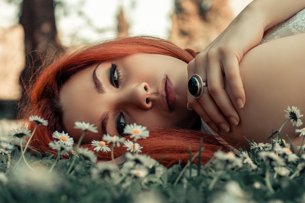 a woman with red hair laying in a field of daisies
