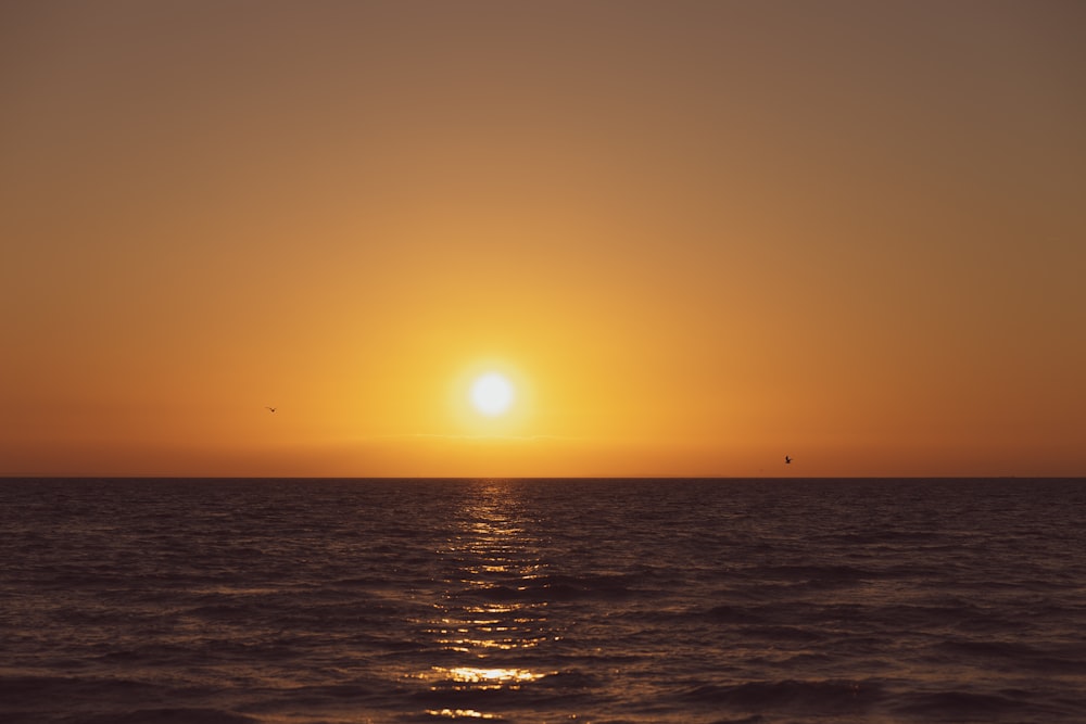 the sun is setting over the ocean with a boat in the distance