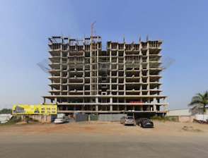 a large building under construction with cars parked in front of it