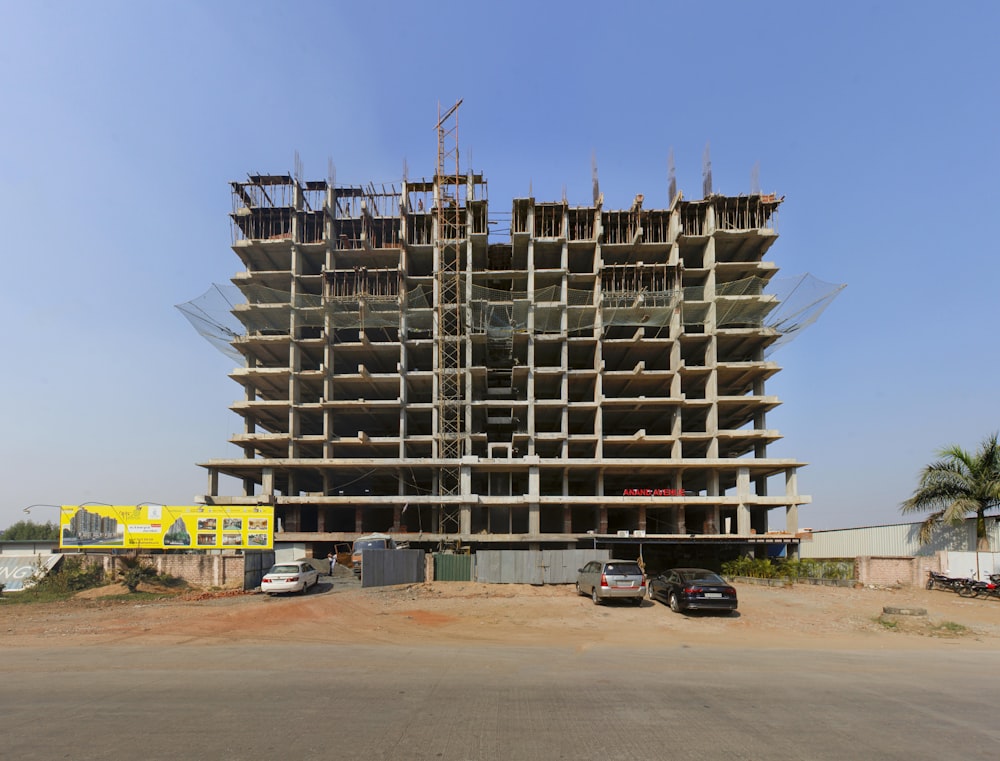 a large building under construction with cars parked in front of it