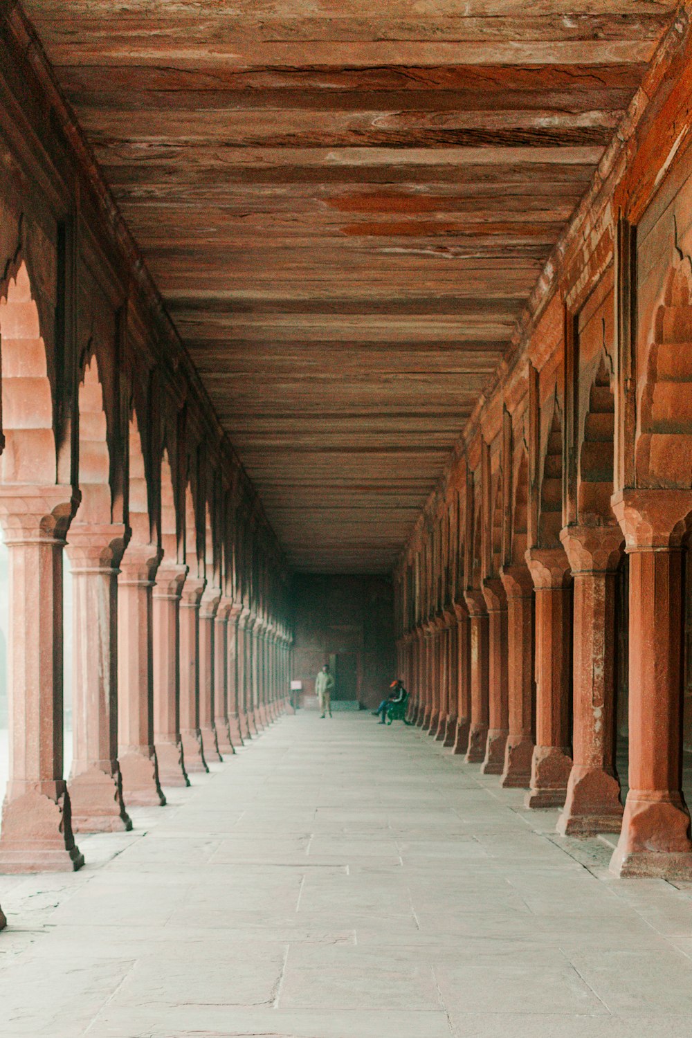 a long hallway with columns and a person sitting on a bench
