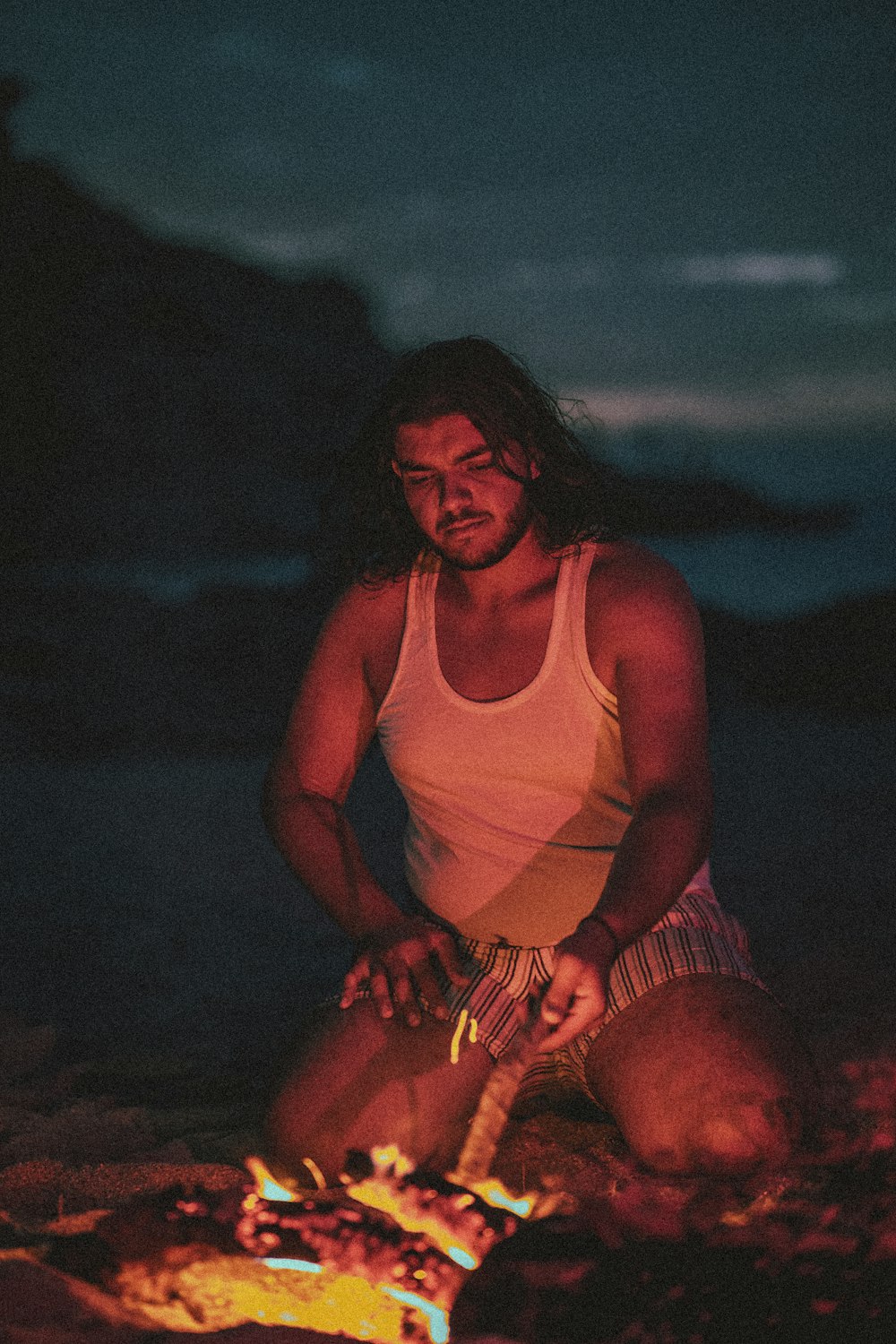 a man with long hair sitting next to a fire