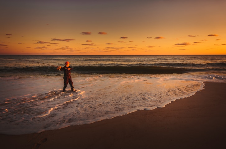 a man standing in the ocean holding a fishing rod