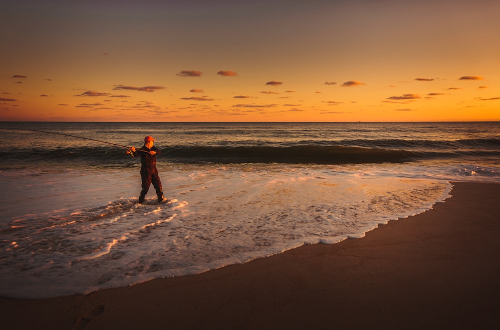 um homem de pé no oceano segurando uma vara de pesca