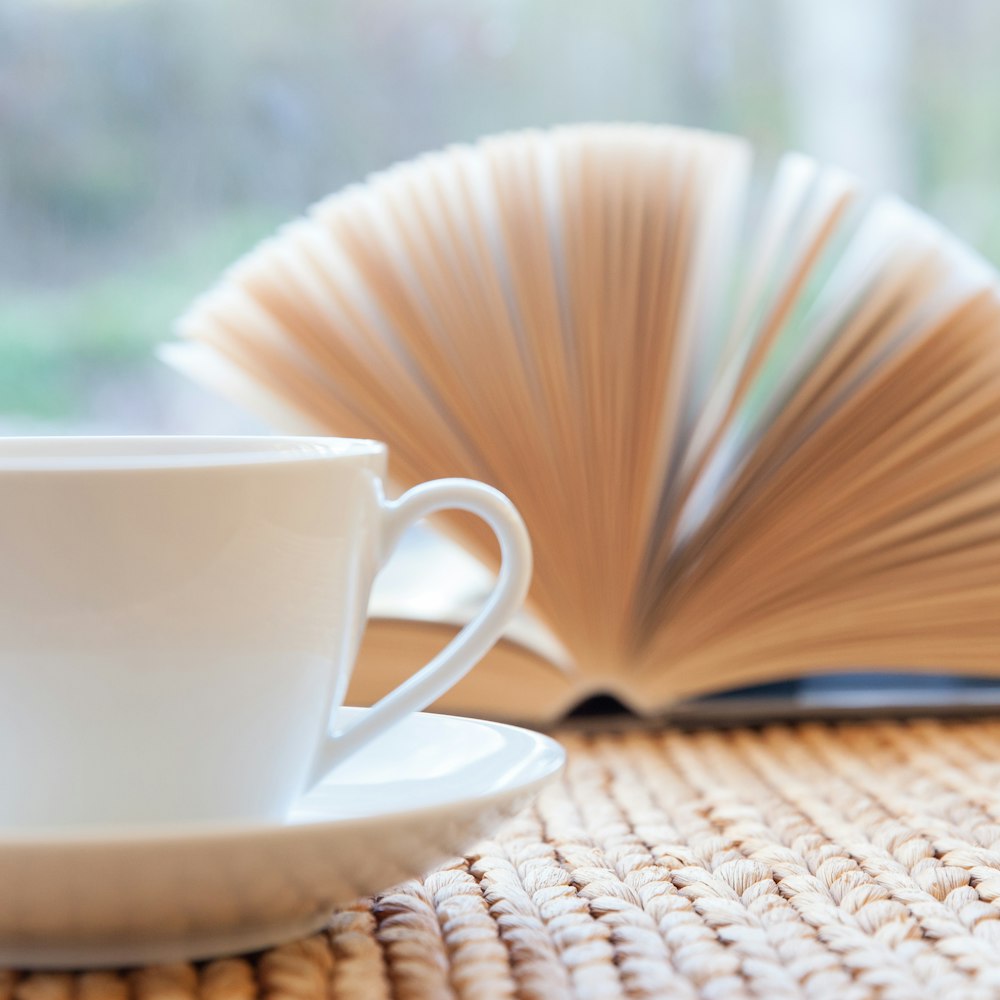 a cup and saucer sitting on a table next to an open book