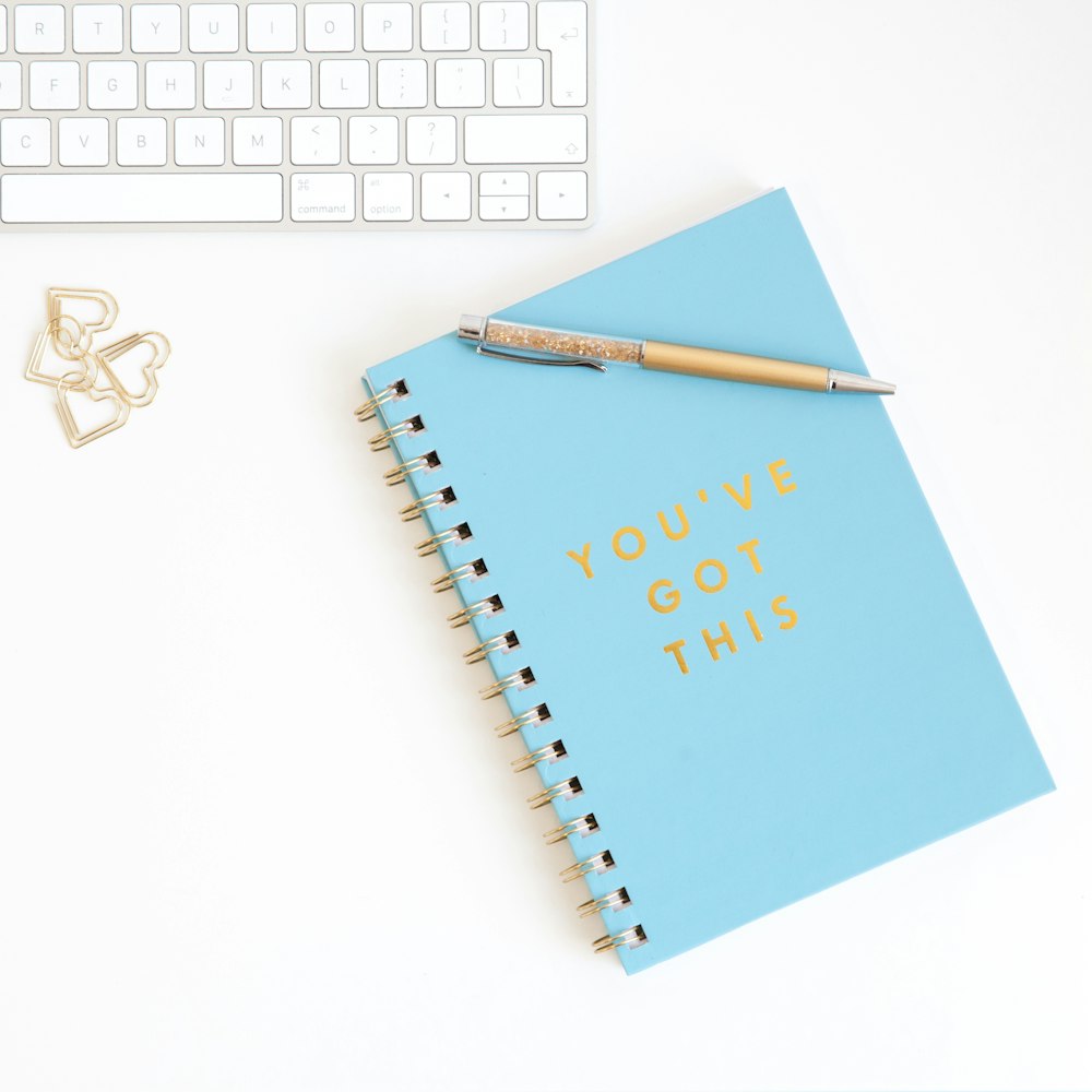 a notepad with a pen on top of it next to a keyboard