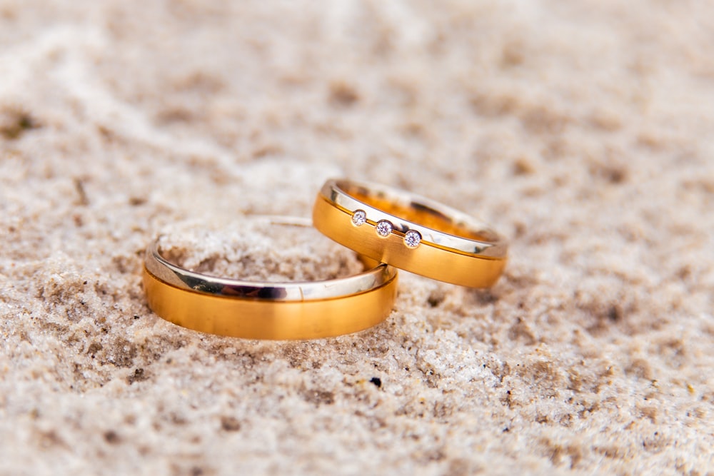 two gold wedding rings laying on the sand