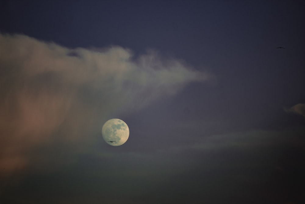 a full moon is seen through a cloudy sky