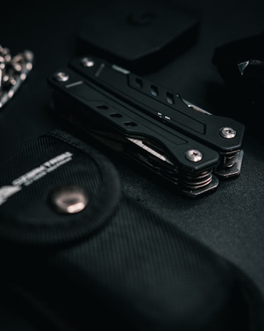 Close-up of a sturdy tactical bottle and compact tool on a dark steel surface with moody lighting.