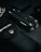 A multitool is surrounded by various dark-colored objects, including a textured black pouch. The scene is set against a dark backdrop, creating a sleek and minimalist aesthetic.