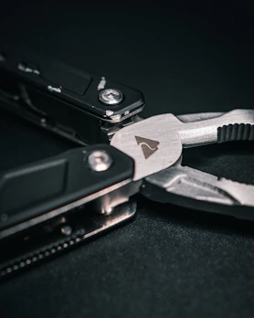 Hand holding a compact multi-tool plier against a bright outdoor background.