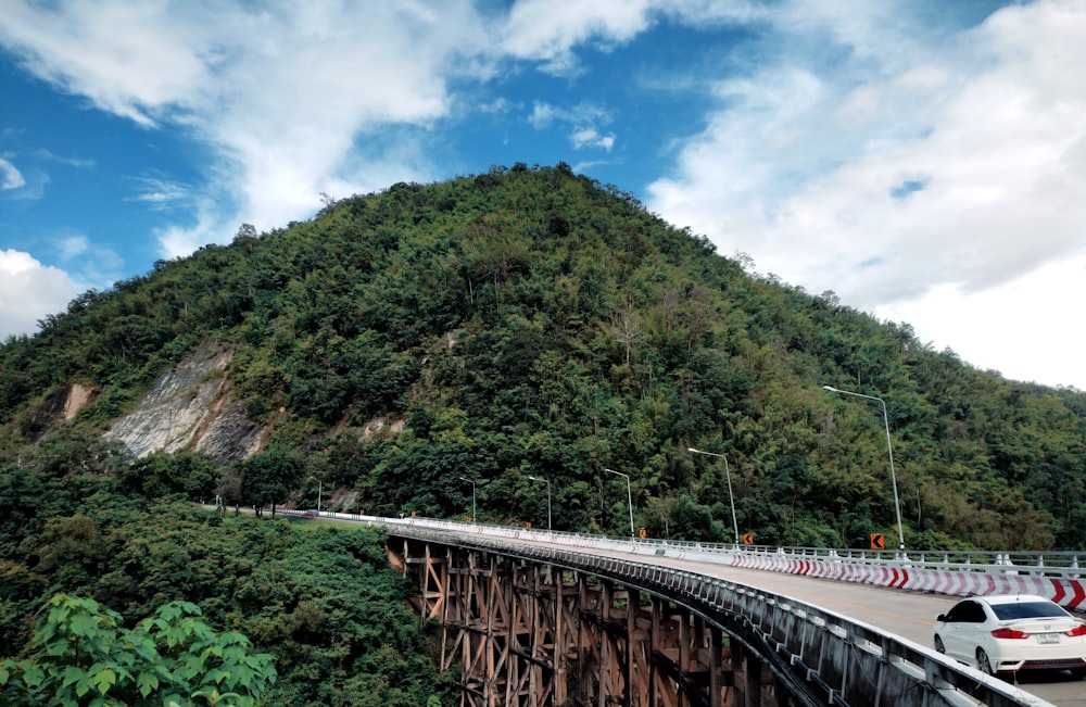 a car driving over a bridge with a mountain in the background