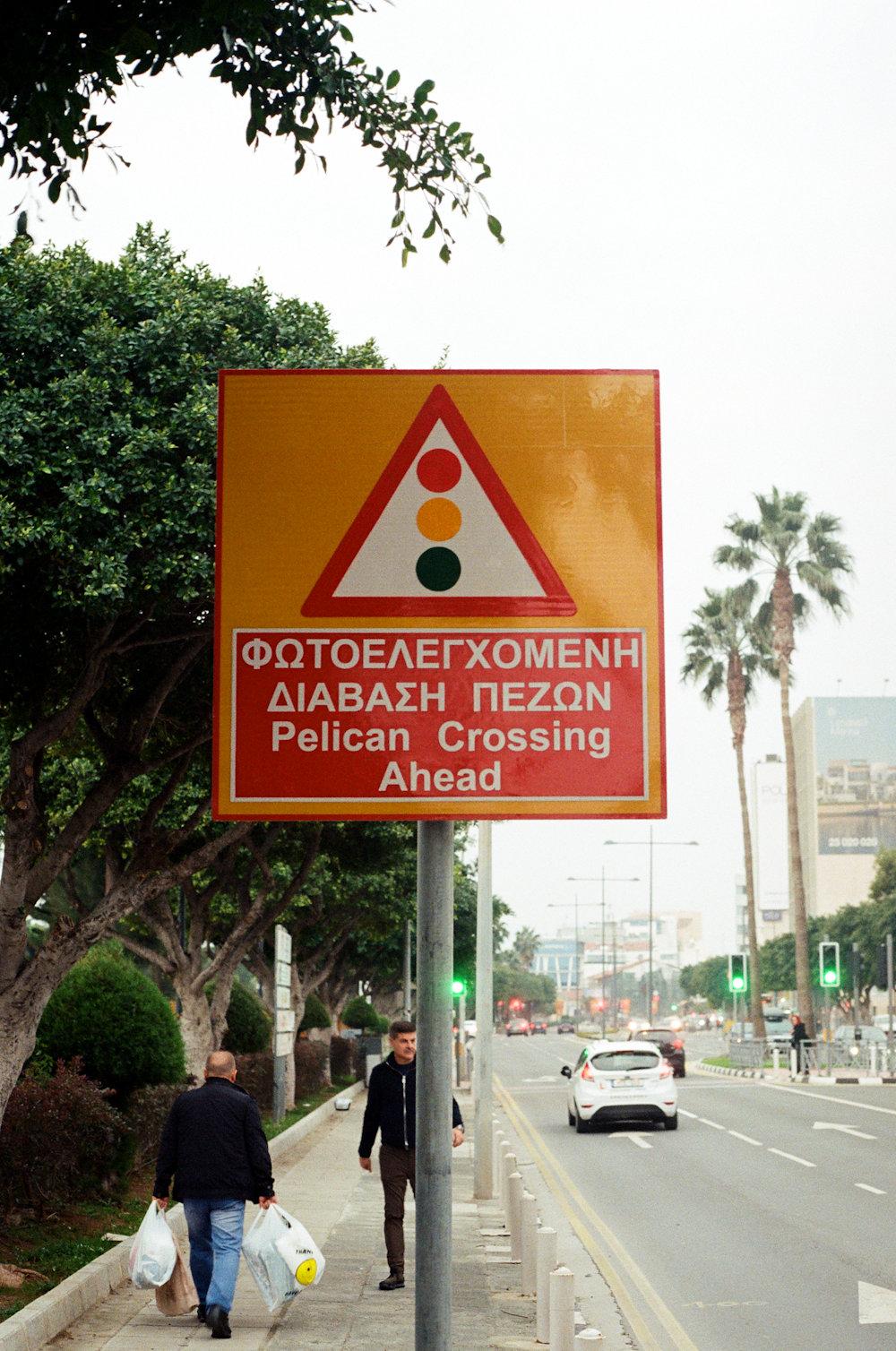 two people walking down a sidewalk next to a street sign