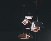 Several pendant lights hang from the ceiling, uniquely designed to resemble open books with light bulbs inside. The lighting fixtures are suspended by cords and are set against a dark background, giving the scene a moody atmosphere.
