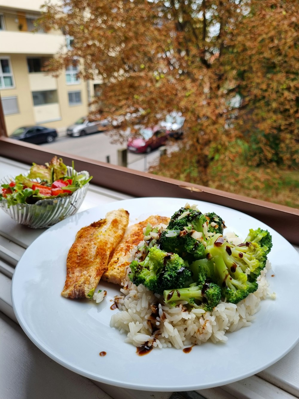 a white plate topped with rice and broccoli next to a bowl of salad