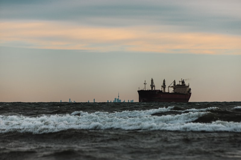Large ship on rough seas at dusk with city skyline in the distance