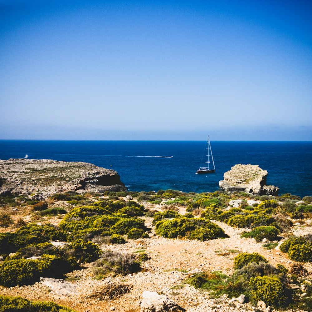 a sailboat is out on the water near a rocky shore