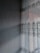 A textured wall with a subtle, embossed pattern is adjacent to a window adorned with sheer lace curtains featuring intricate floral designs. Sunlight filters through the curtains, casting delicate shadows and patterns on the wall.