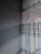 A textured wall with a subtle, embossed pattern is adjacent to a window adorned with sheer lace curtains featuring intricate floral designs. Sunlight filters through the curtains, casting delicate shadows and patterns on the wall.
