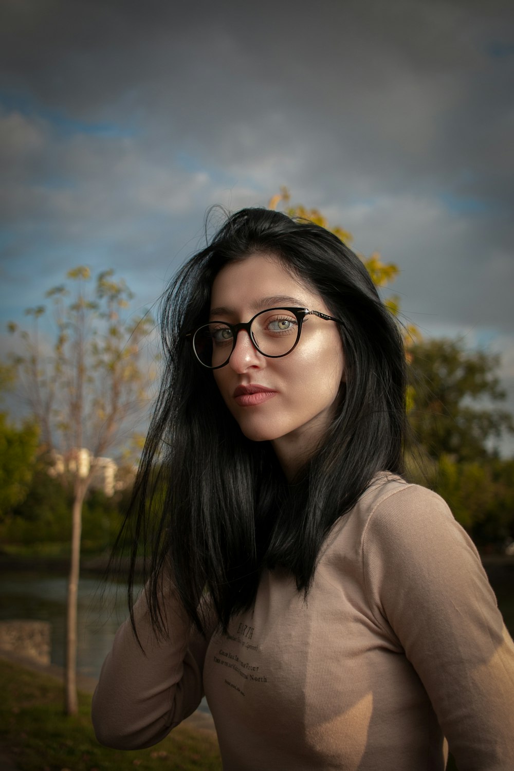 a woman wearing glasses standing in front of a body of water