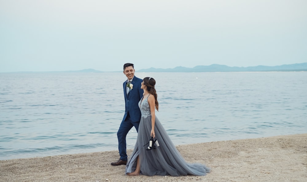 a man and woman standing on a beach next to the ocean