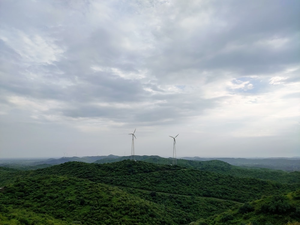 three windmills on a hill with a cloudy sky