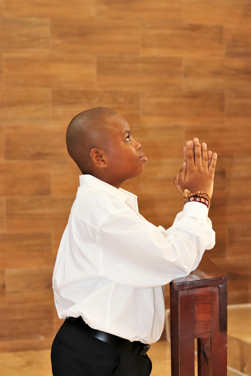a young boy in a white shirt and black pants praying