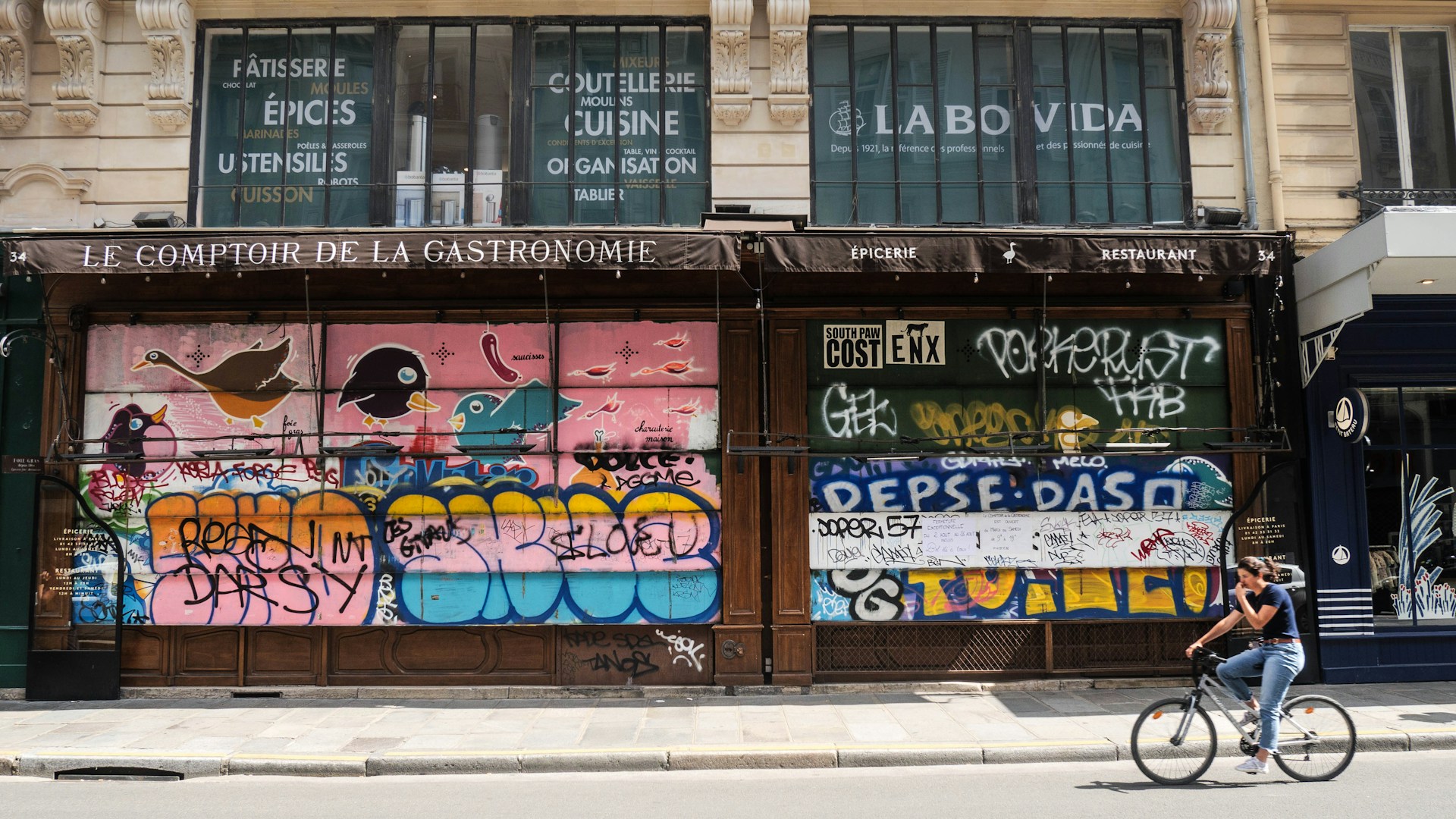 a man riding a bike past a building covered in graffiti