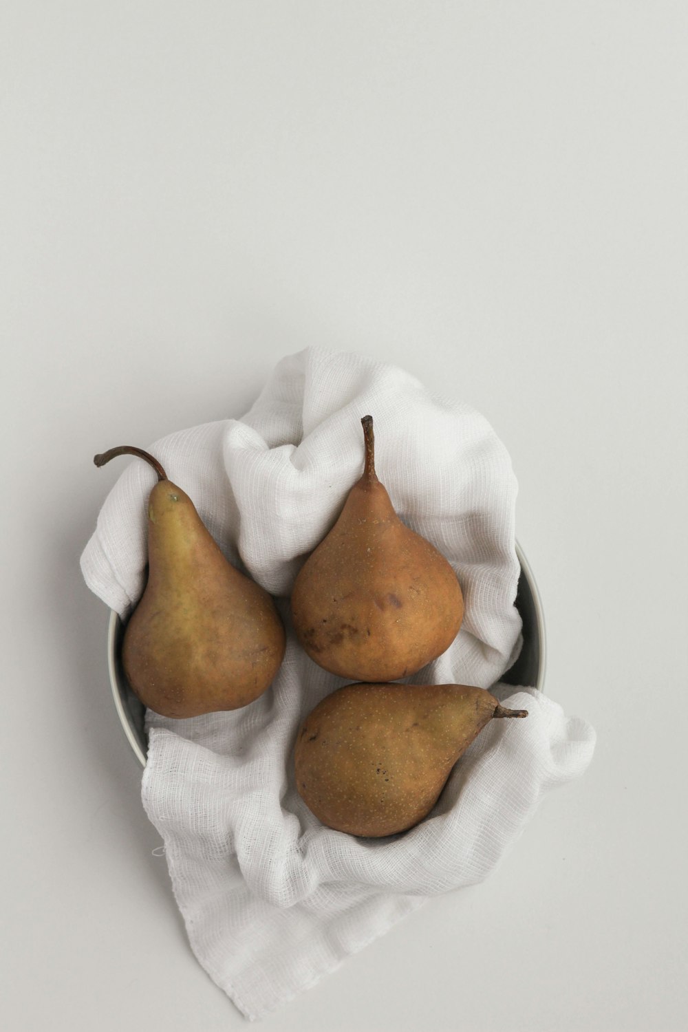 three pears in a bowl on a white cloth