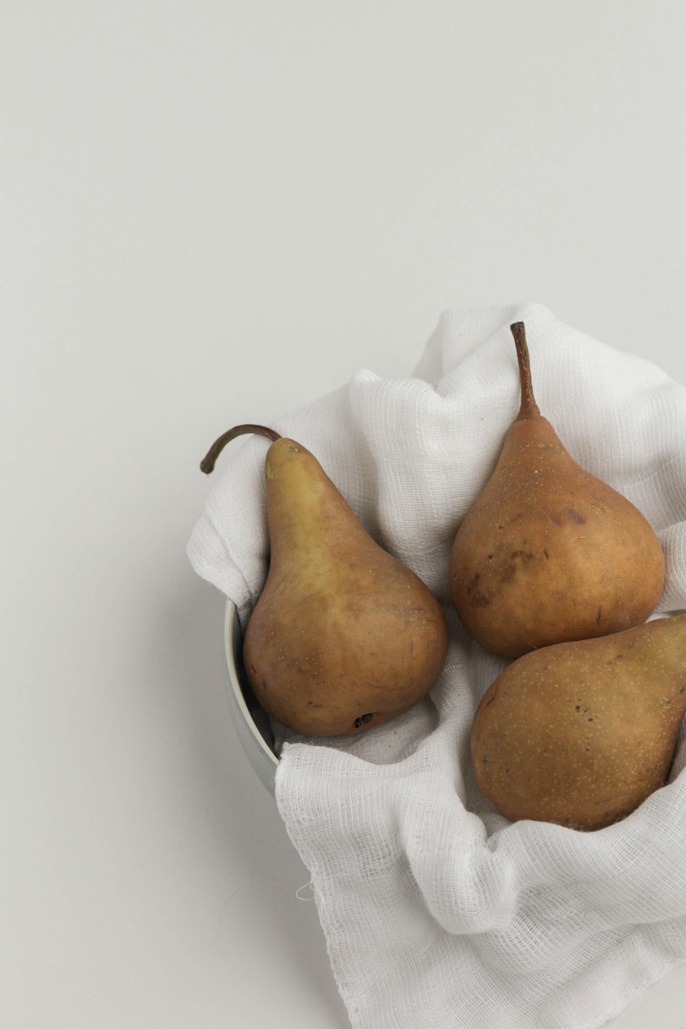 four pears in a bowl on a white cloth