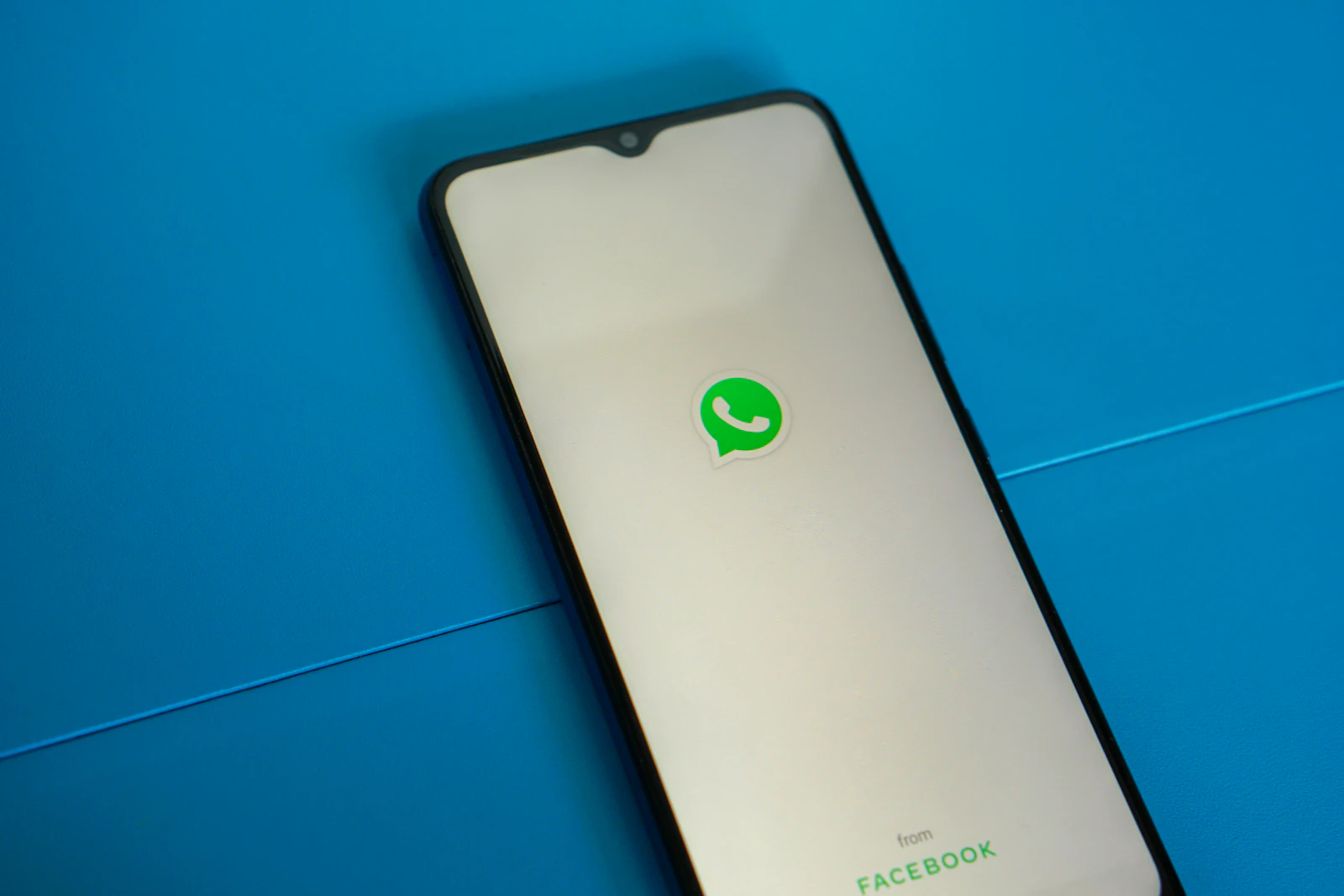 A smartphone with a WhatsApp logo on screen lying on a blue surface