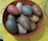 A collection of large, oval-shaped stones with a speckled texture is arranged inside a round, brown container with handles. The stones vary in colors such as grey, brown, and beige. The container is resting on a yellow surface.