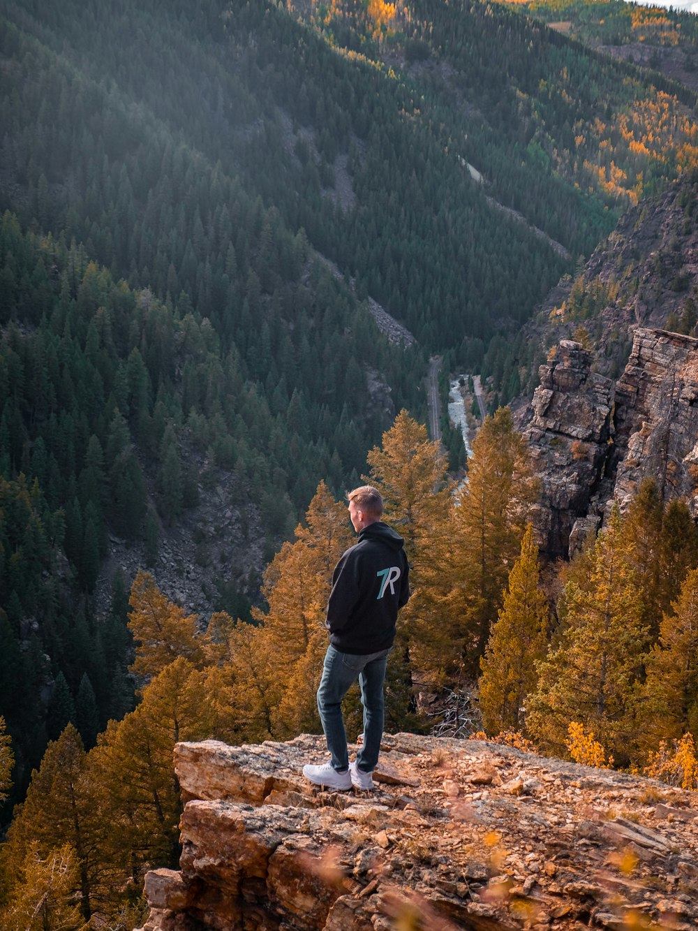 a man standing on top of a cliff next to a forest
