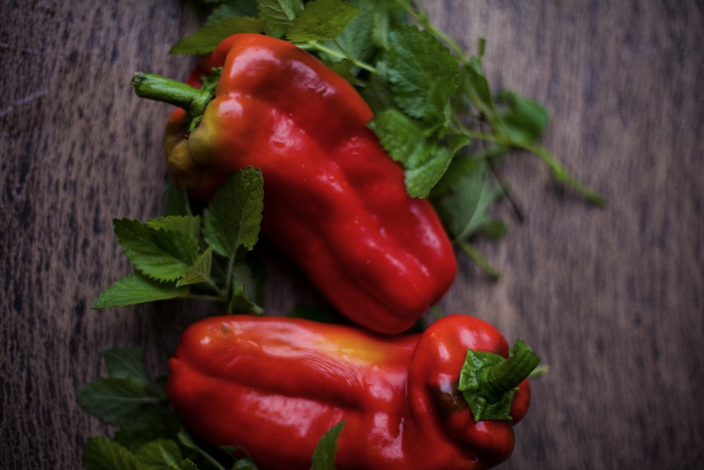 Tres pimientos rojos con hojas verdes sobre una superficie de madera