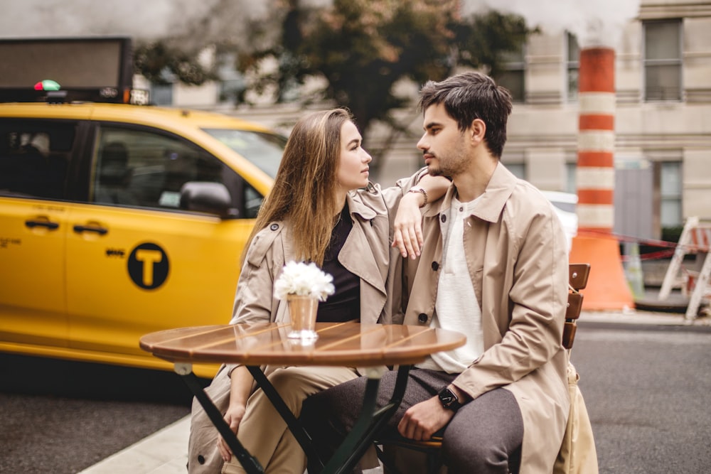 a man and a woman sitting at a table in front of a taxi