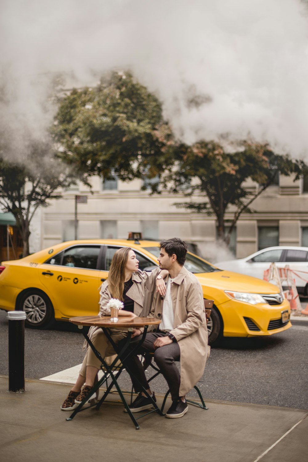 a man and woman sitting at a table in front of a yellow taxi