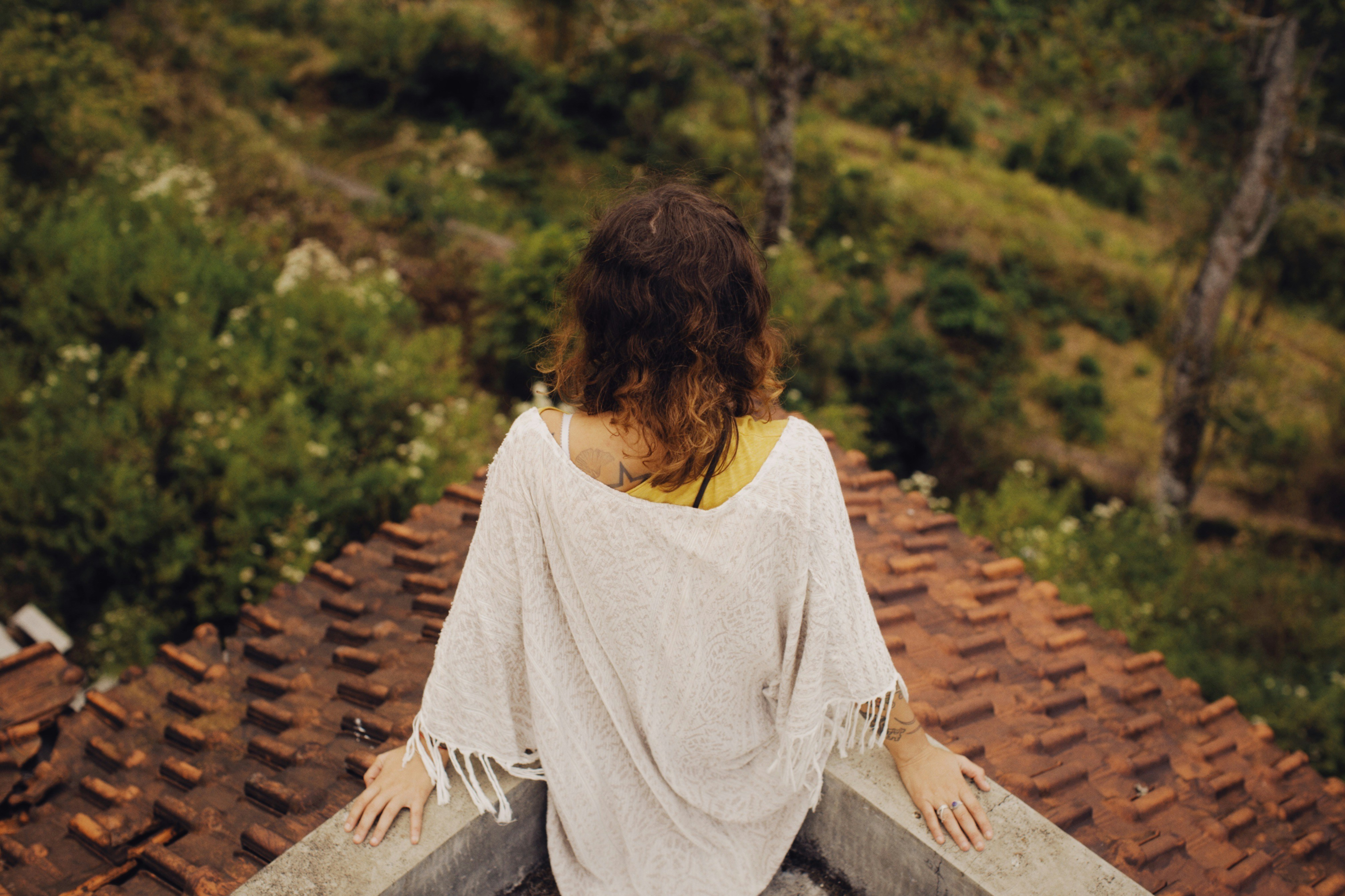 a woman sitting on top of a roof next to a forest