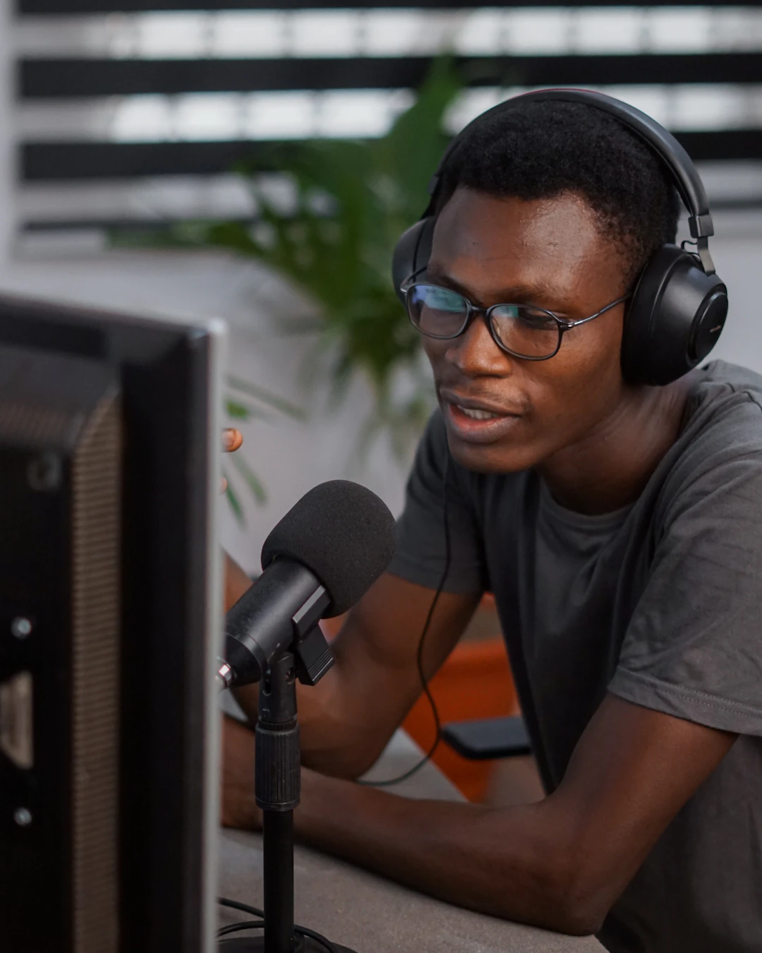 A person wearing headphones and talking into a microphone at a home-office desk